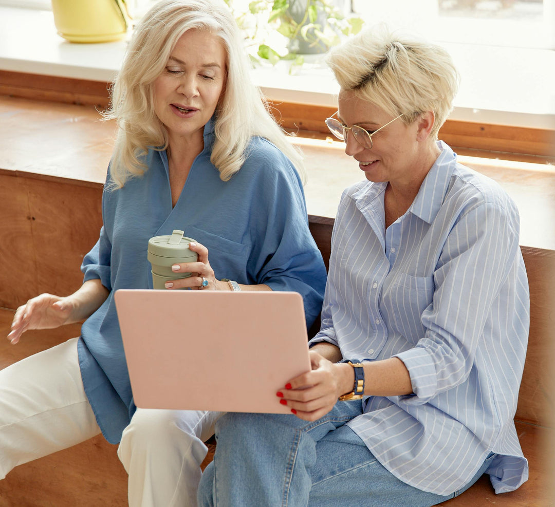 Two women sitting together looking at a laptop in a home setting.